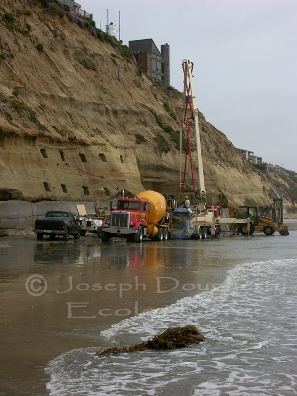 Construction crew creating concrete seawall to bolster sandstone cliffs and control coastal erosion.