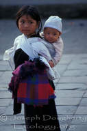 Indigenous girl with baby sister strapped to her back.